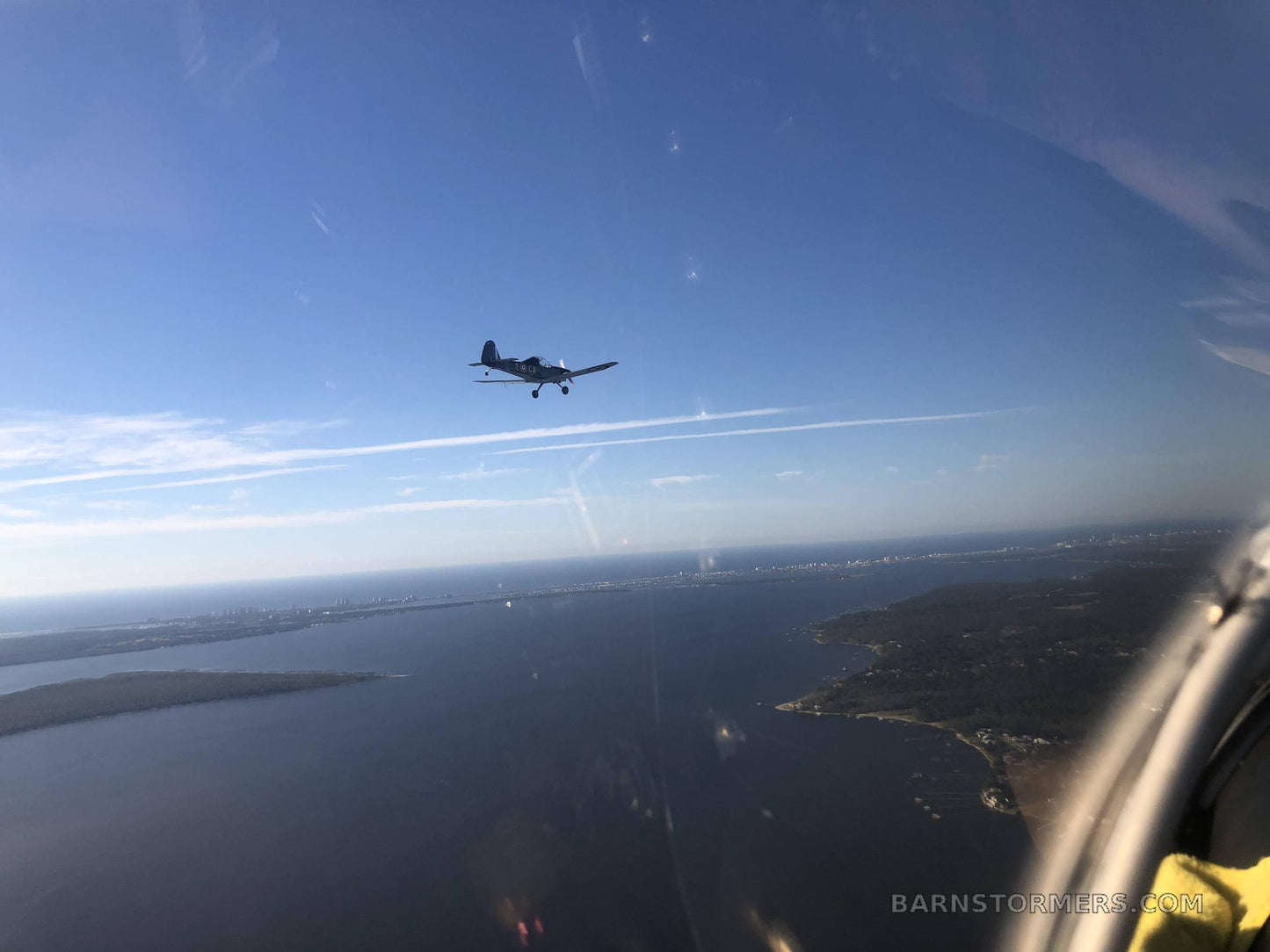 Small airplane flying over a coastal landscape with a clear blue sky.