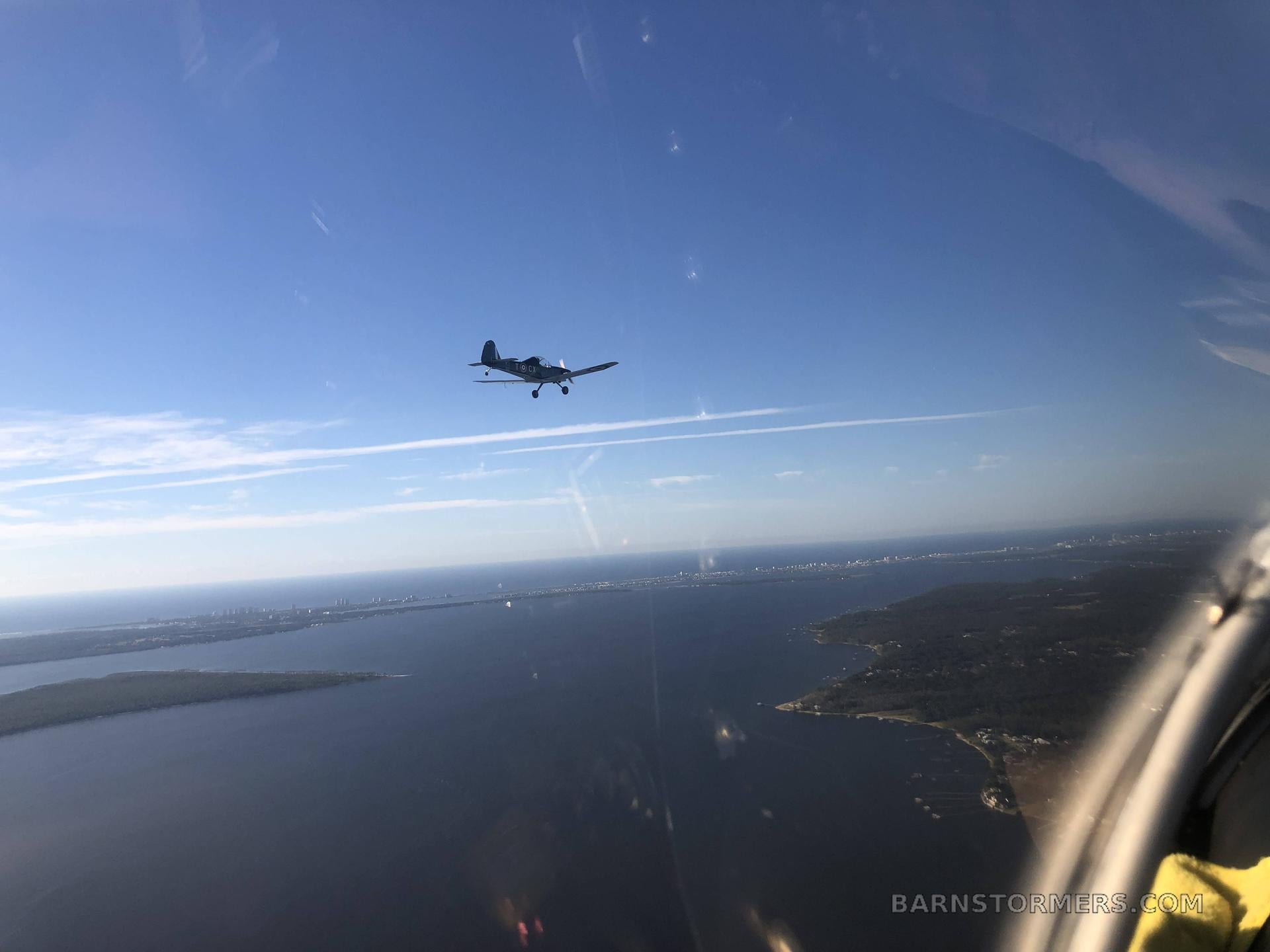 Small airplane flying over a coastal landscape with a clear blue sky.